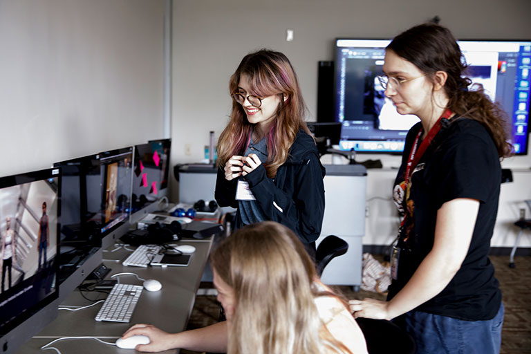 Three women looking at a computer screen where a video game is being designed.